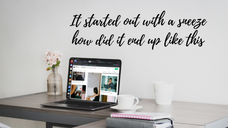 A laptop on a table showing images of people in work from home situations, surrounded by mugs and a flower vase. Writing on the wall behind shows "It started out with a sneeze how did it end up like this?"